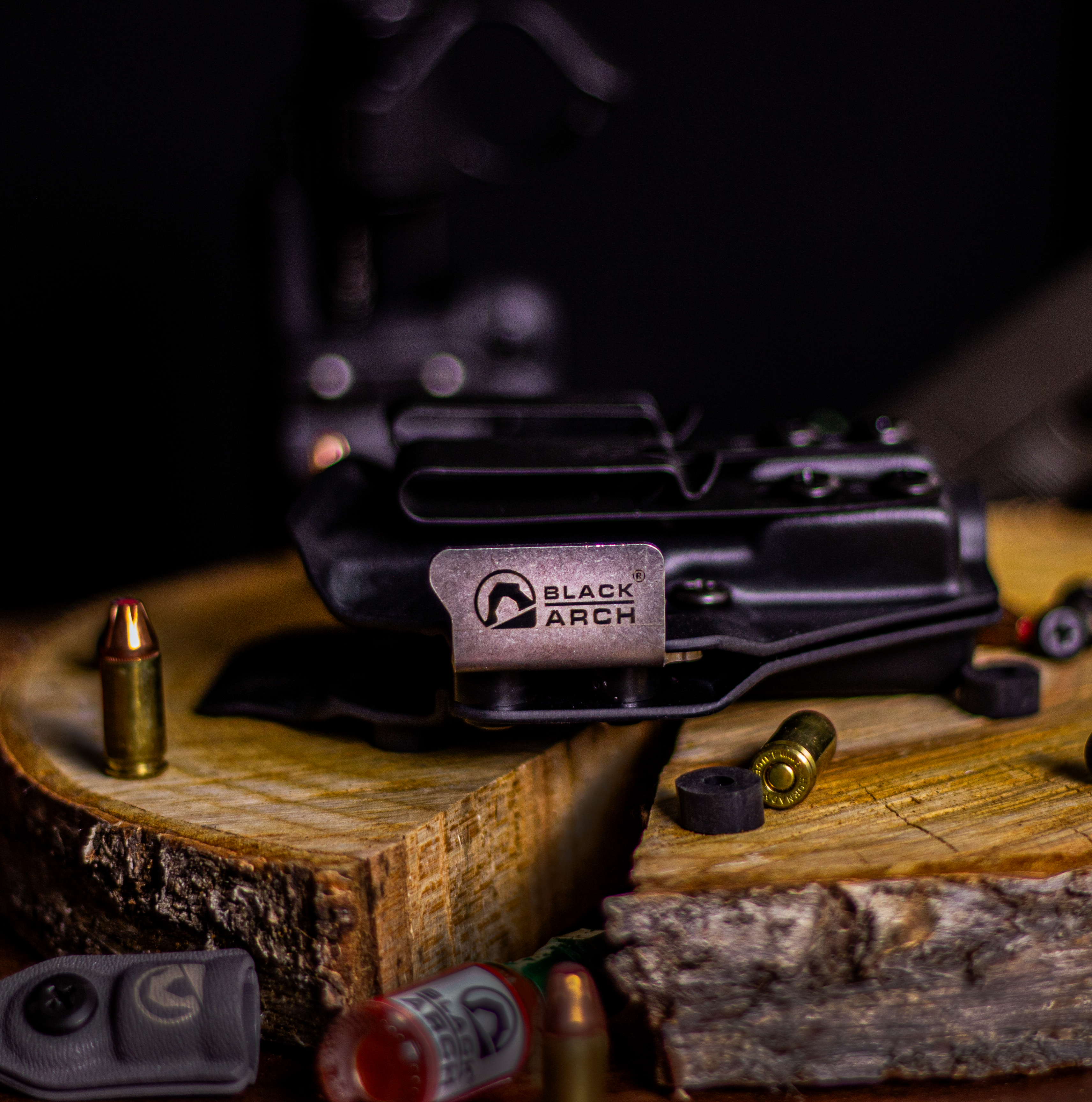 Square image of a right-hand Gradient Minimalist holster for Glock 19 with Black Arch metal clip, displayed on a wood slab with scattered rounds and accessories.